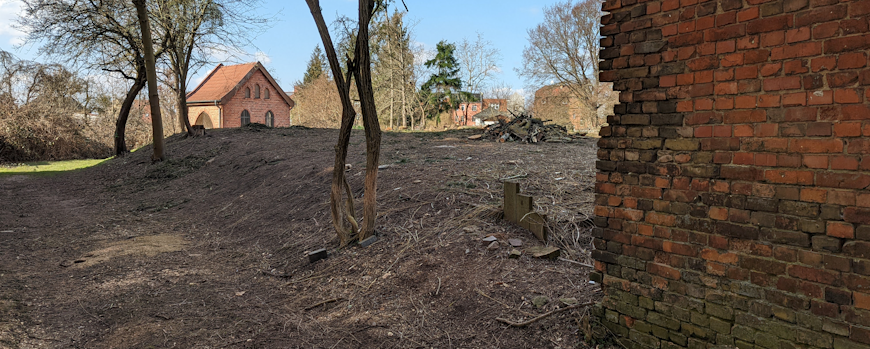 Blick auf die freigelegte Leichenwagenhalle hinter den noch benutzten ehemaligen Scheunen; März 2022