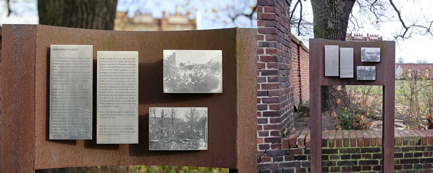 Informationstafel zur Geschichte des Ortes am Rand der Friedhofsmauer.